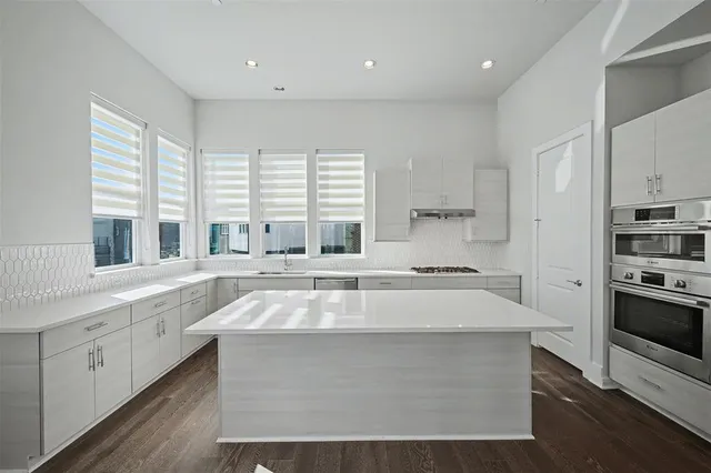 a large white kitchen with stainless steel appliances granite countertop a stove and a large window