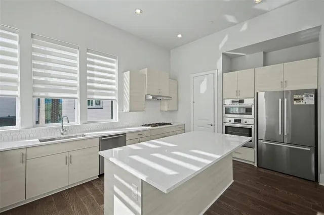 a kitchen that has a lot of white cabinets and stainless steel appliances