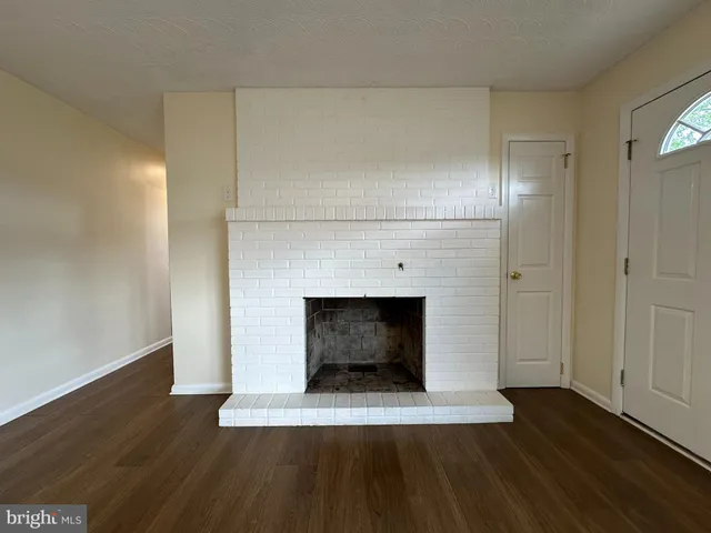 a view of an empty room with wooden floor and a fireplace