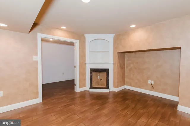 an empty room with wooden floor and way to kitchen