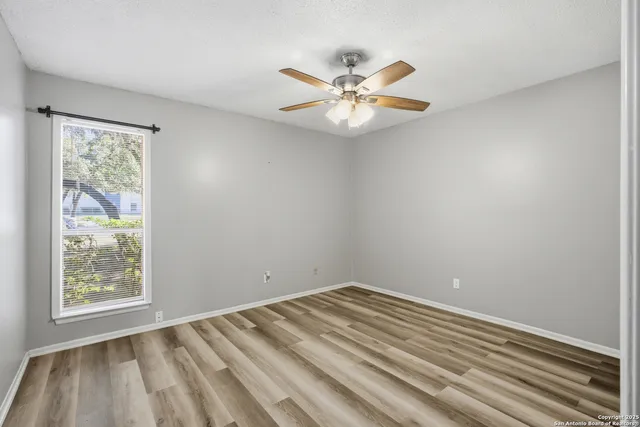 a view of an empty room with chandelier fan and wooden floor