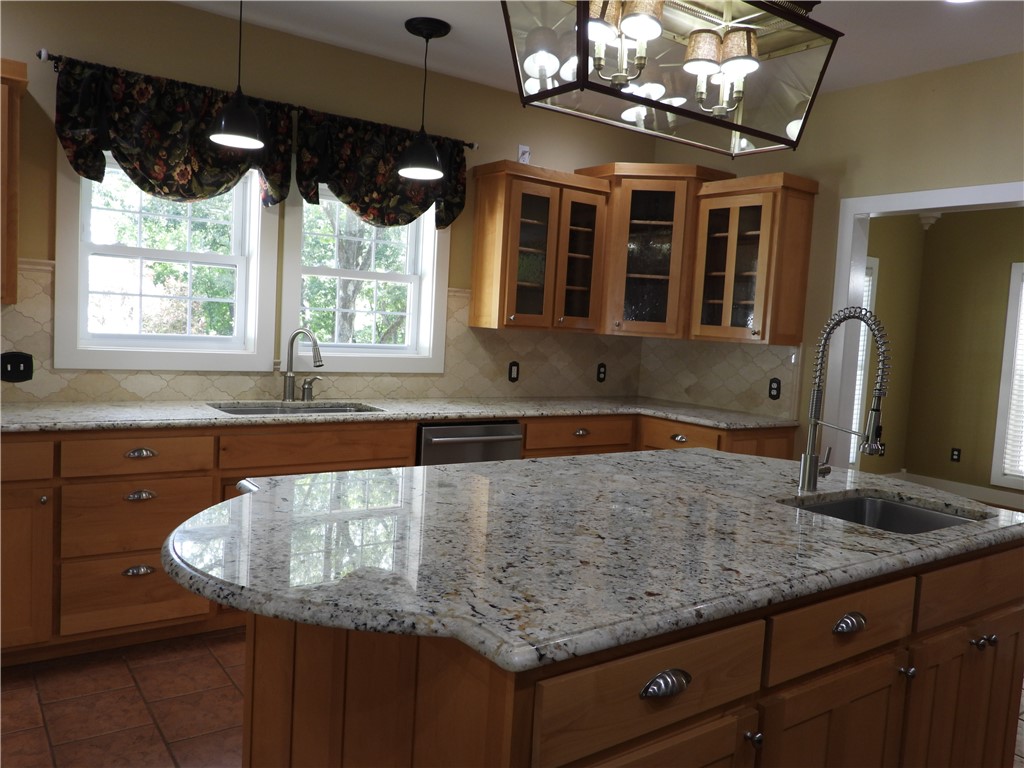 19489 Oak Circle Springdale, AR 72764 - Photo 9 of 58 Kitchen featuring an island with an undermount sink and gooseneck faucet, garage disposal, granite countertops, tile backsplash, and tile flooring