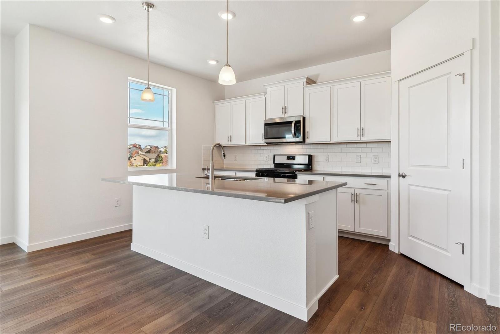 2220 Base Street Fort Lupton, CO 80621 - Photo 11 of 36 a kitchen with kitchen island white cabinets and wooden floor