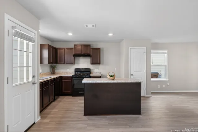 a kitchen with stainless steel appliances kitchen island granite countertop a stove top oven a sink dishwasher a refrigerator and cabinets with wooden floor