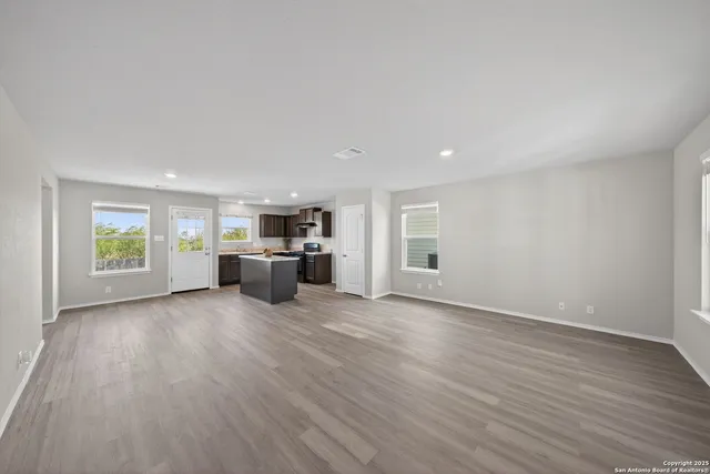 a big room with wooden floor kitchen electric appliances and windows