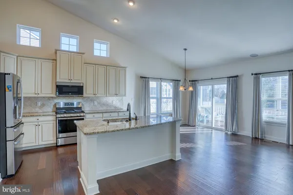 a kitchen with stainless steel appliances granite countertop a stove a sink dishwasher a refrigerator and white cabinets with wooden floor