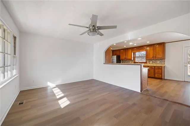 an empty room with wooden floor kitchen view and windows