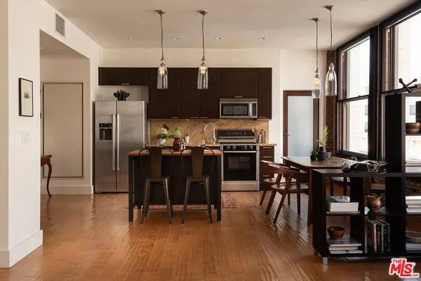 a kitchen with stainless steel appliances a refrigerator a stove top oven a sink dishwasher and a dining table with wooden floor