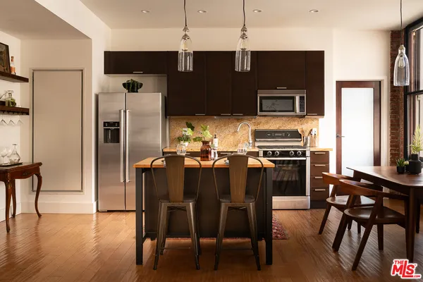 a kitchen with stainless steel appliances a refrigerator a stove a microwave oven a dining table and chairs with wooden floor