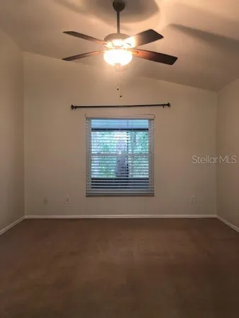 an empty room with a chandelier fan and windows