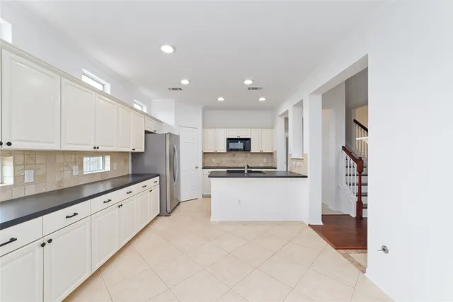 a large kitchen with stainless steel appliances kitchen island a sink dishwasher a refrigerator and white cabinets with wooden floor