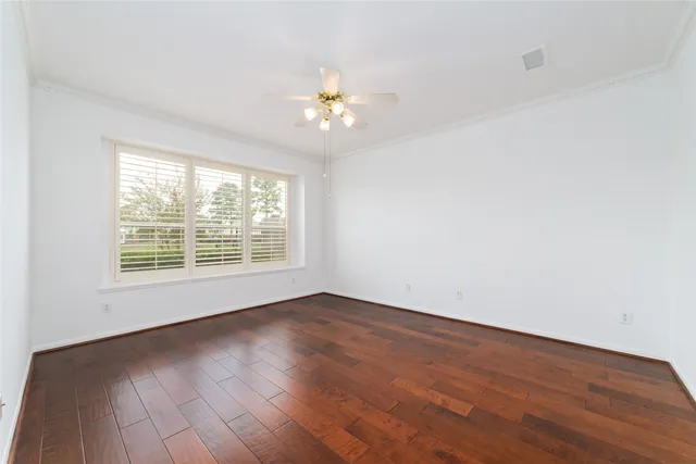 an empty room with wooden floor chandelier fan and windows