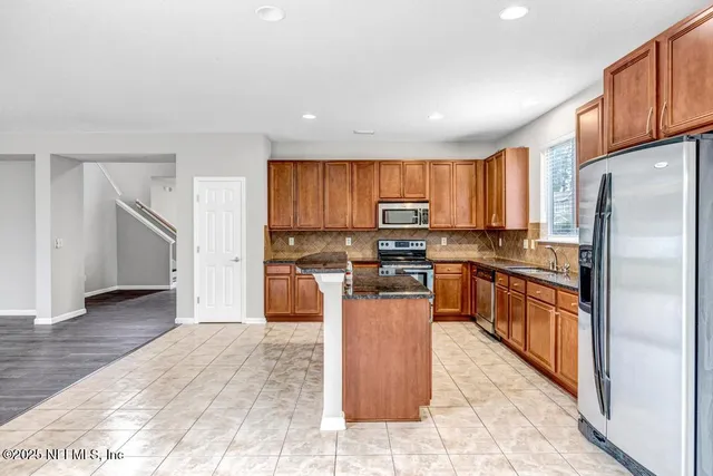 a kitchen with stainless steel appliances granite countertop a refrigerator oven a sink a stove a dining table and chairs