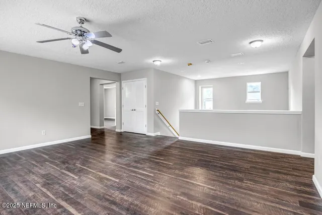 a view of an empty room with wooden floor and a ceiling fan