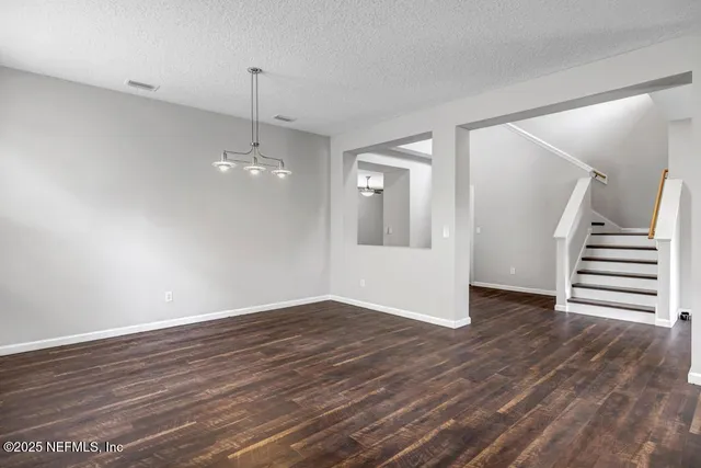 a view of an empty room with wooden floor and stairs