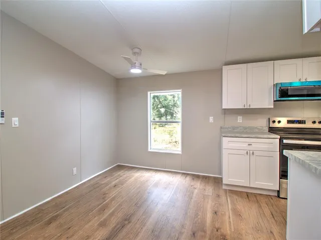 a kitchen with granite countertop a stove a sink and white cabinets with wooden floor next to windows