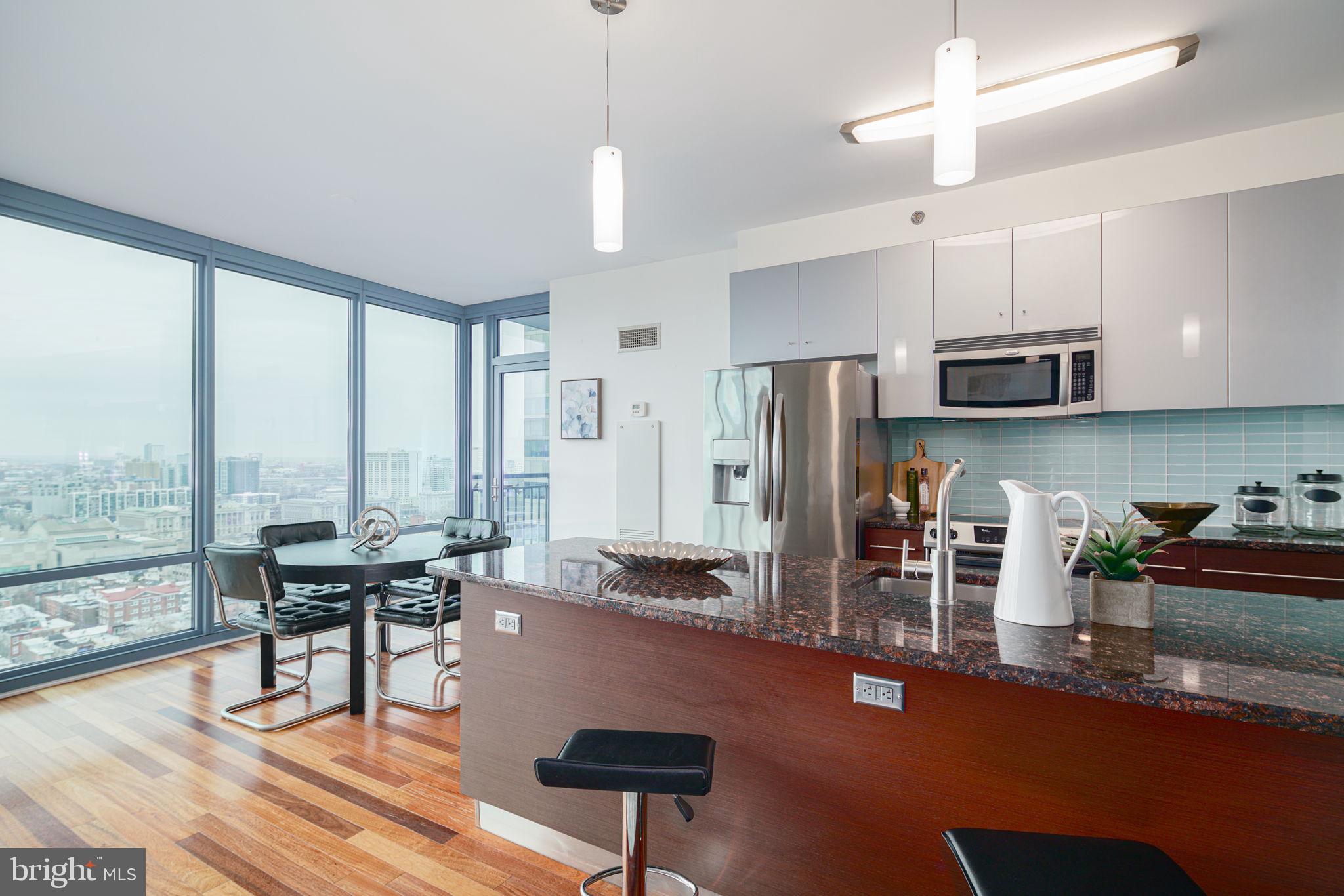 2101 Market Street, Unit 1901 Philadelphia, PA 19103 - Photo 7 of 25 a kitchen with stainless steel appliances granite countertop a stove a refrigerator a sink a dining table and chairs with wooden floor