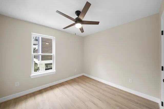 an empty room with wooden floor ceiling fan and windows