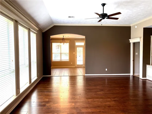an empty room with wooden floor chandelier fan and windows