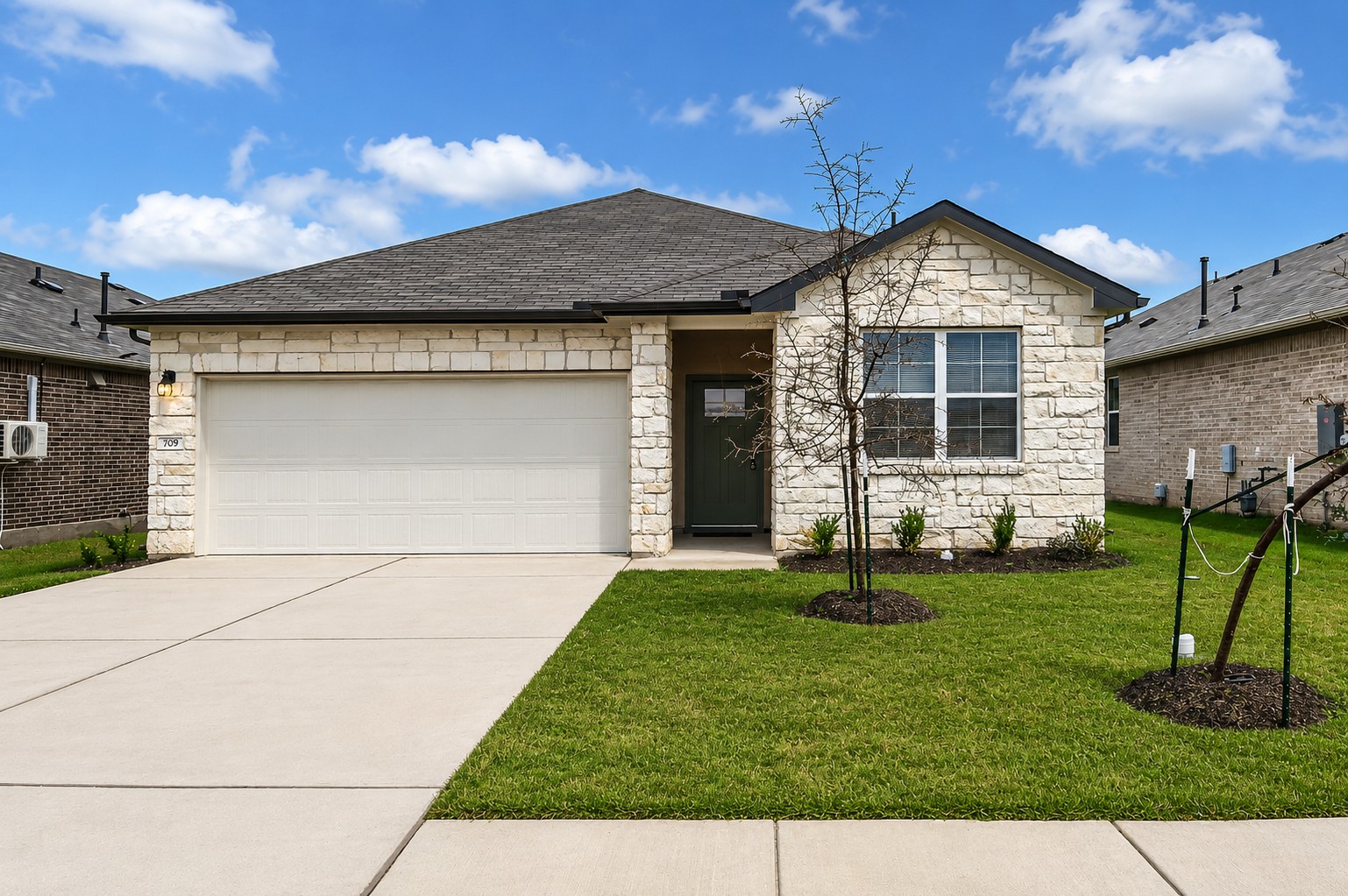 A well-maintained lawn and concrete driveway welcome you to this charming single-story residence with a stone facade.