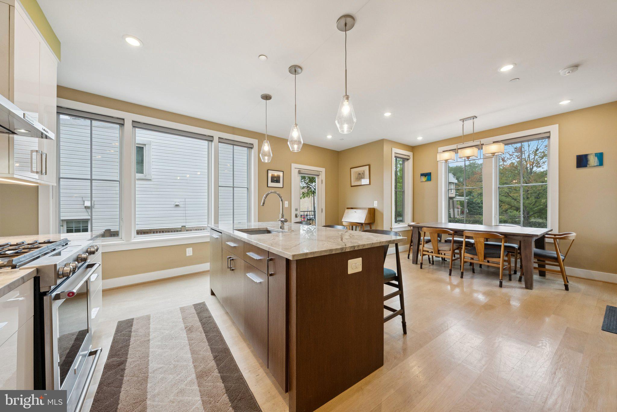 a kitchen with kitchen island granite countertop a stove a sink a dining table and chairs with wooden floor
