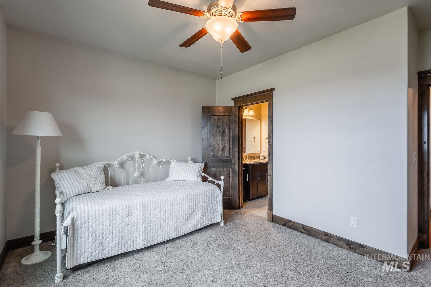8077 Star Pass Ridge Road Nampa, ID 83686 - Photo 29 of 37 Plush carpeted room featuring a ceiling fan with light fixture, light gray walls, dark wood trim, and a visible doorway leading to a bathroom with a vanity and mirror