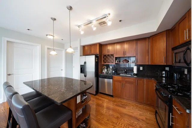 a kitchen with stainless steel appliances granite countertop a stove refrigerator a sink a dining table and chairs with wooden floor