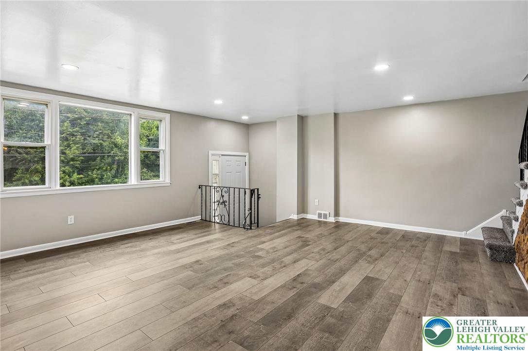 A spacious, naturally illuminated room features light wood flooring and a classic wrought iron railing.