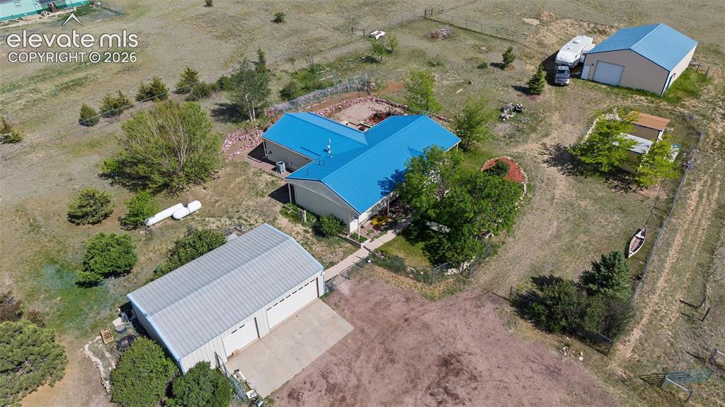 13075 Blaney Road South Peyton, CO 80831 - Photo 2 of 40 Expansive property featuring a main residence with a blue metal roof, a detached two-bay garage with concrete pad, barn with blue metal roof, and a separate fenced area for horses with established trees