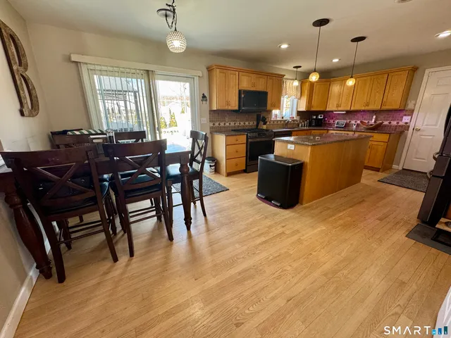 a kitchen with stainless steel appliances kitchen island granite countertop a stove a refrigerator a kitchen island a stove a dining table and chairs with wooden floor
