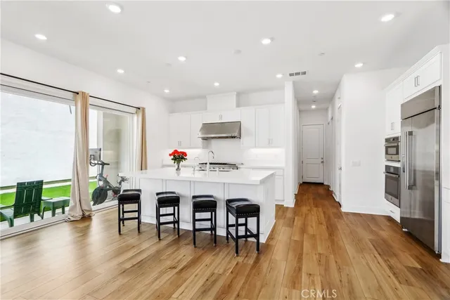 a living room with stainless steel appliances furniture wooden floor and a kitchen view