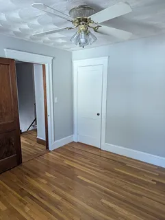 a view of an empty room with wooden floor and a ceiling fan