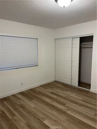 a view of a refrigerator in kitchen and an empty room with wooden floor