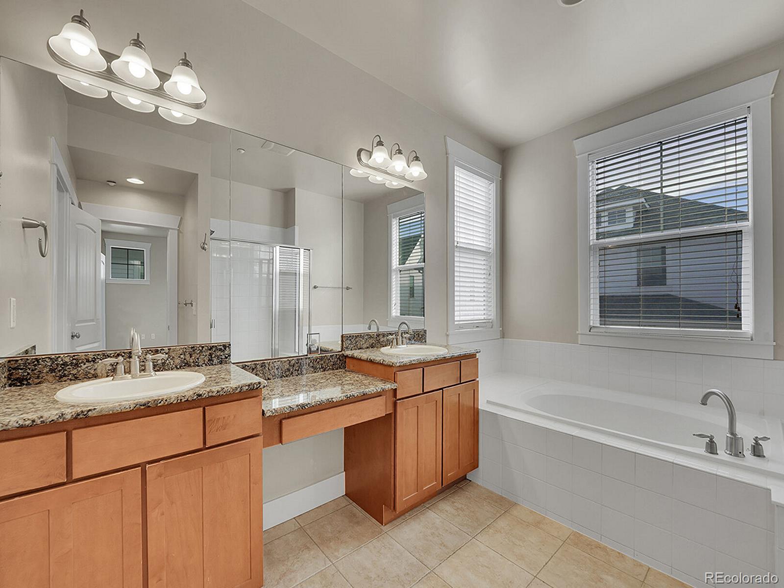 11718 Perry Street Westminster, CO 80031 - Photo 11 of 15 a bathroom with a granite countertop sink a large mirror and a bathtub with shower