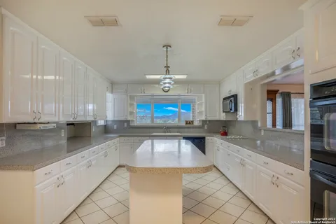 a large kitchen with granite countertop a sink and white cabinets