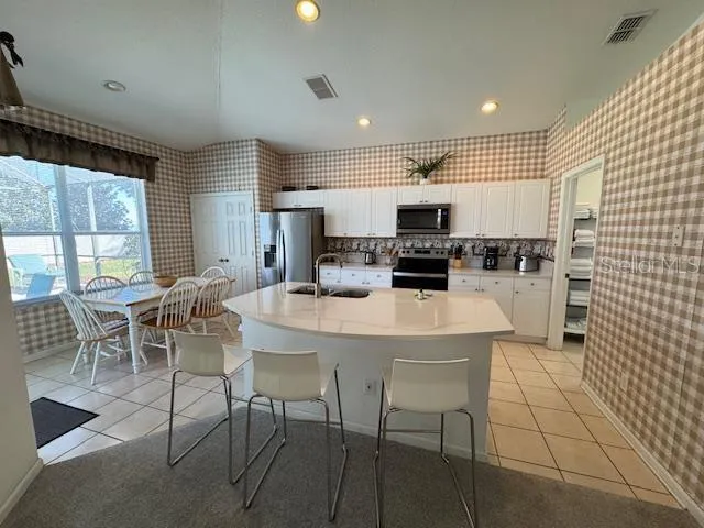 a kitchen with stainless steel appliances kitchen island granite countertop a dining table chairs and a refrigerator