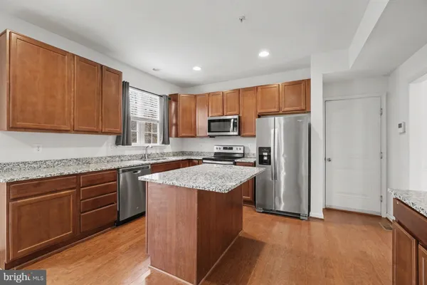 a view of kitchen with stainless steel appliances granite countertop a stove top oven a refrigerator and a sink with wooden floor