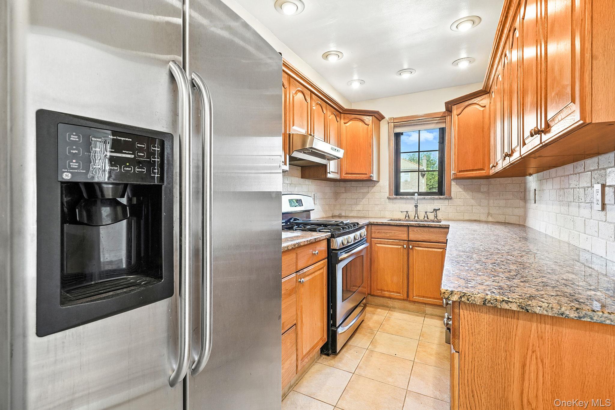 1245 Rhinelander Avenue Bronx, NY 10461 - Photo 13 of 34 Kitchen with appliances with stainless steel finishes, backsplash, light stone countertops, light tile patterned floors, and brown cabinetry