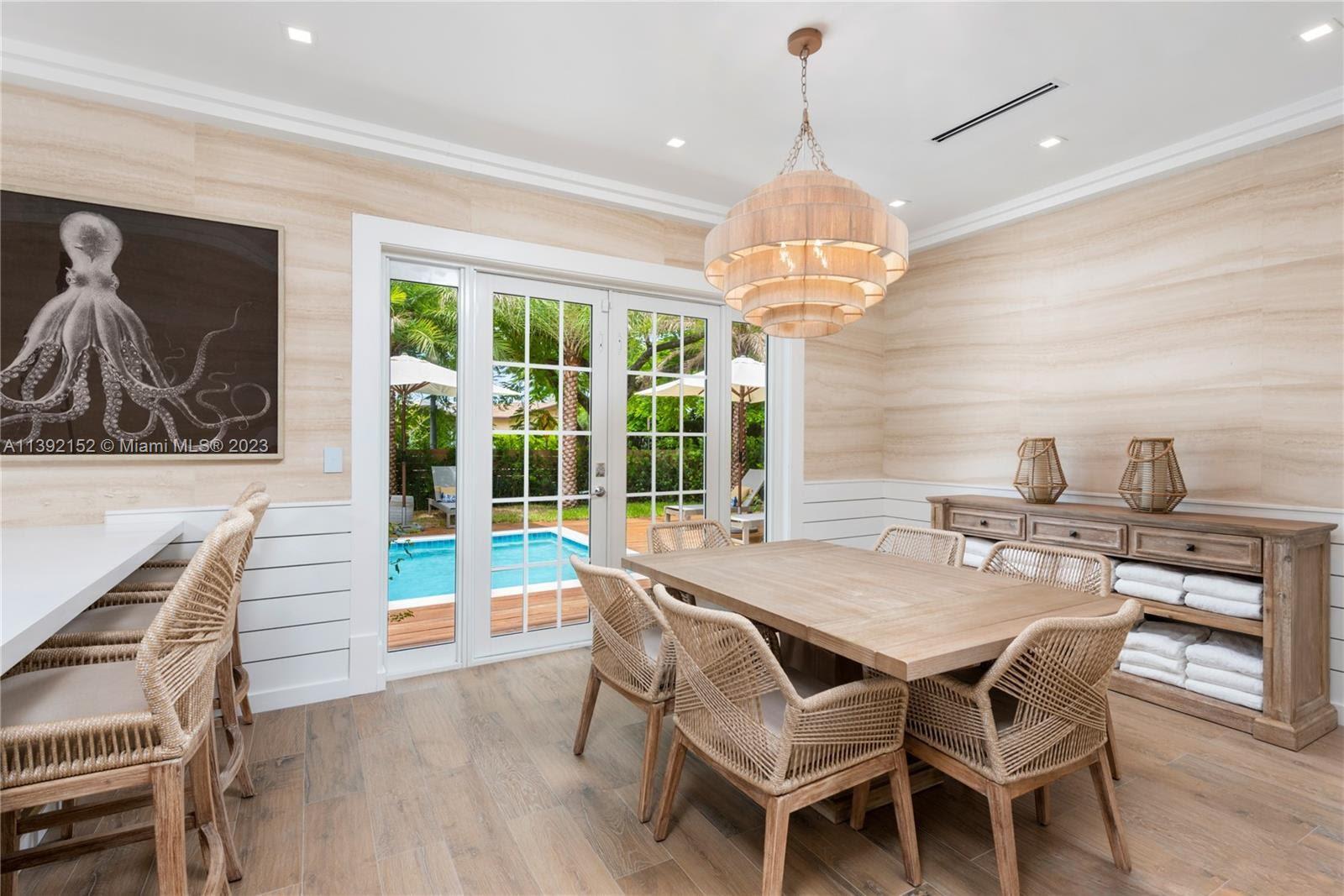 2575 Pine Tree Drive Miami Beach, FL 33140 - Photo 23 of 37 a dining room with wooden floor a chandelier a wooden table and chairs