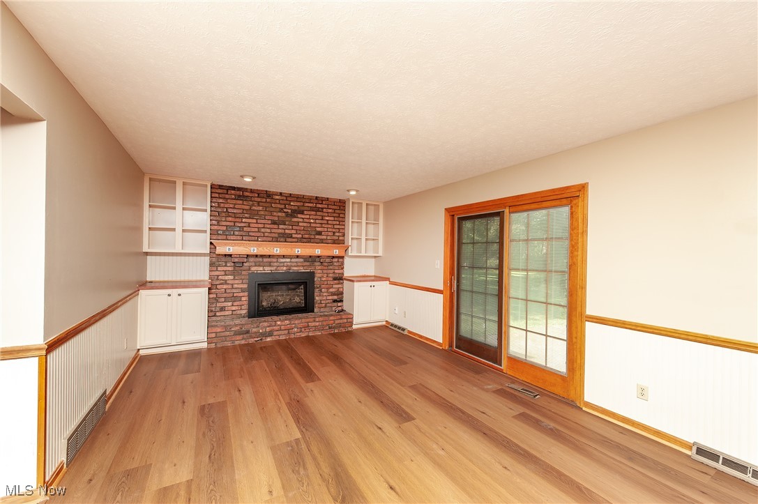 27680 Dunford Road Westlake, OH 44145 - Photo 9 of 31 Unfurnished living room featuring light wood-type flooring, a brick fireplace, built in shelves, and a textured ceiling