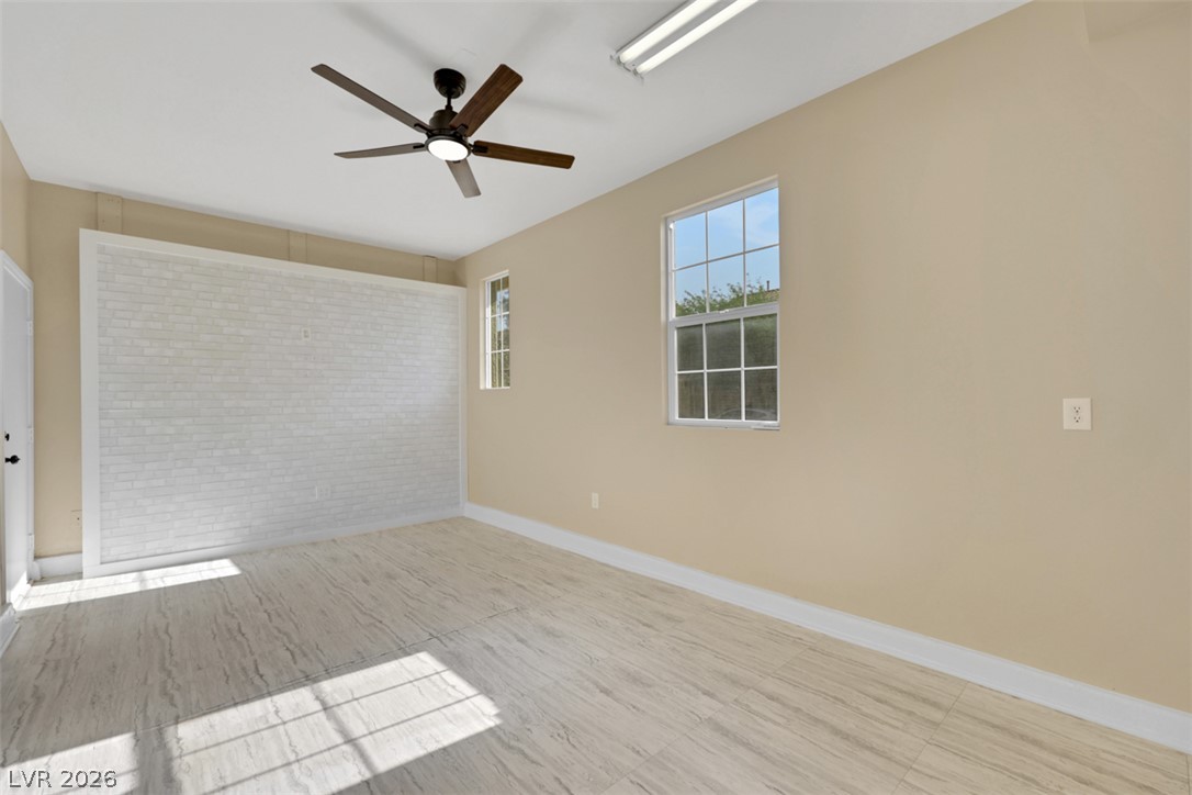 10328 Hawk Ravine Street Las Vegas, NV 89178 - Photo 51 of 55 A well-lit, neutral-toned room features wood-look flooring and a distinctive white brick accent wall.