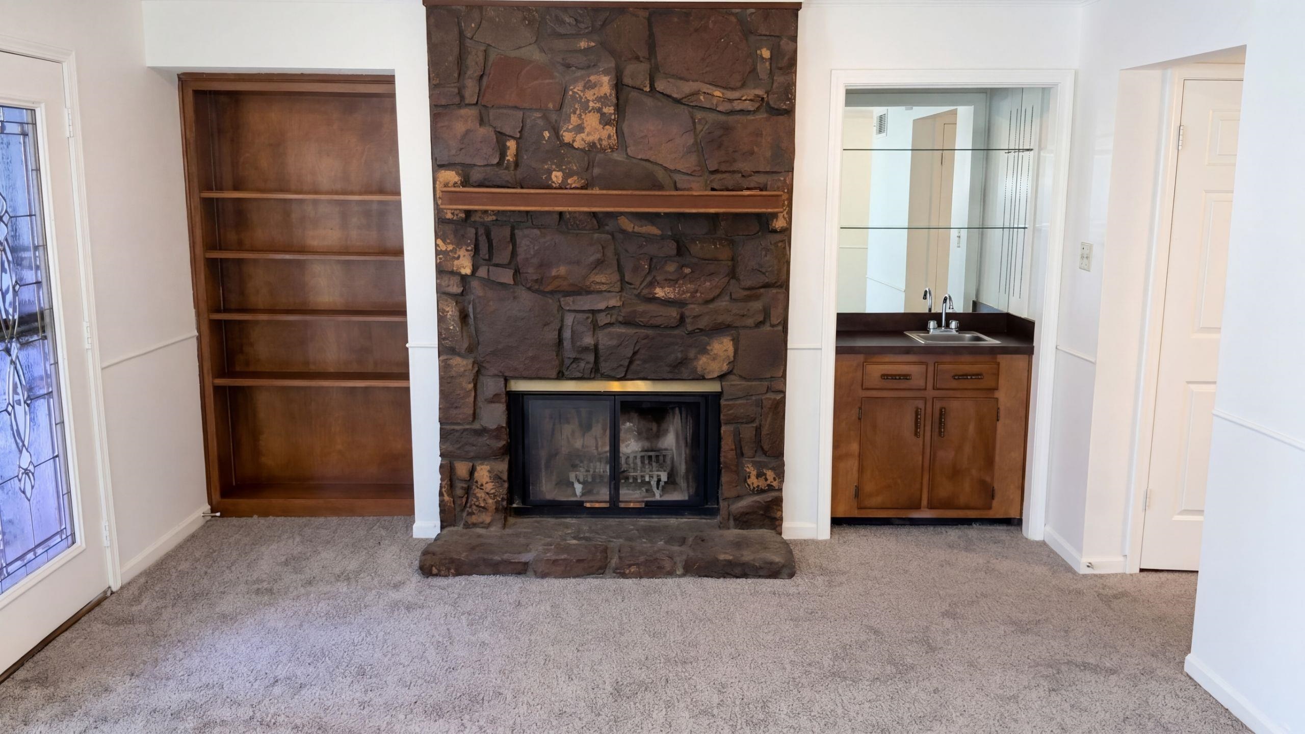 3798 Fern Ridge Road Memphis, TN 38115 - Photo 8 of 16 Stone-clad fireplace with a wood mantle, built-in wooden shelving, and a wet bar with an integrated sink and mirrored back