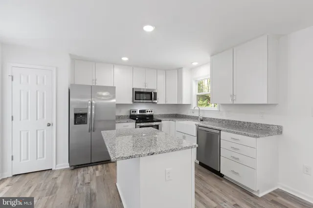 a kitchen with kitchen island a sink dishwasher a stove and white cabinets with wooden floor