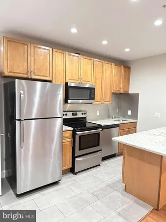 a kitchen with granite countertop a refrigerator a sink a stove a microwave and wooden cabinets