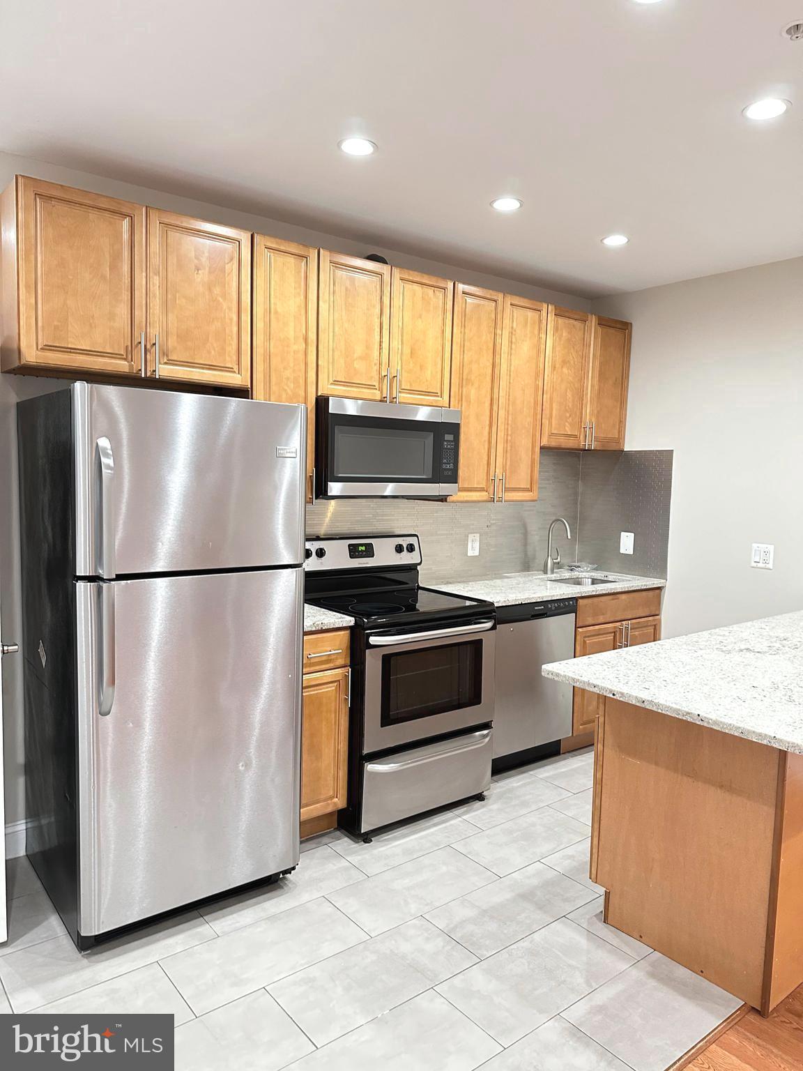 1626 R Street Southeast, Unit 1 Washington, DC 20020 - Photo 9 of 17 a kitchen with granite countertop a refrigerator a sink a stove a microwave and wooden cabinets