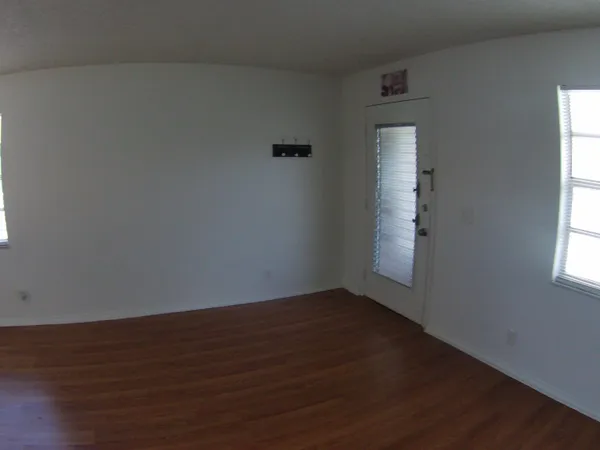an empty room with wooden floor and windows with curtains