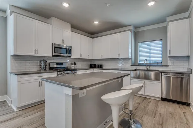 a kitchen with stainless steel appliances granite countertop a sink dishwasher a stove top oven a refrigerator with white cabinets and wooden floor
