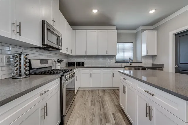 a kitchen with stainless steel appliances granite countertop a stove a sink dishwasher and a microwave oven with white cabinets