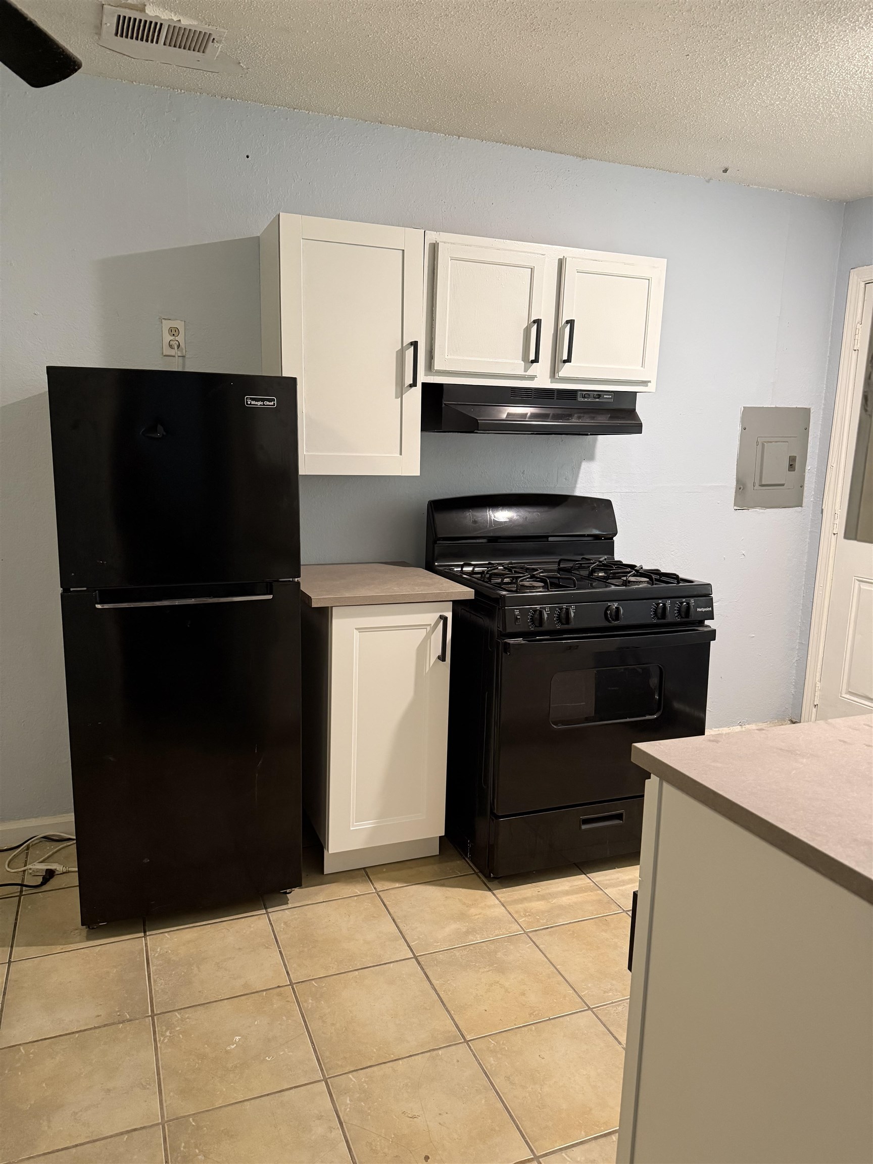 1248 Meda Street Memphis, TN 38114 - Photo 21 of 24 Kitchen featuring black appliances, white cabinets, light tile patterned flooring, a textured ceiling, and light countertops