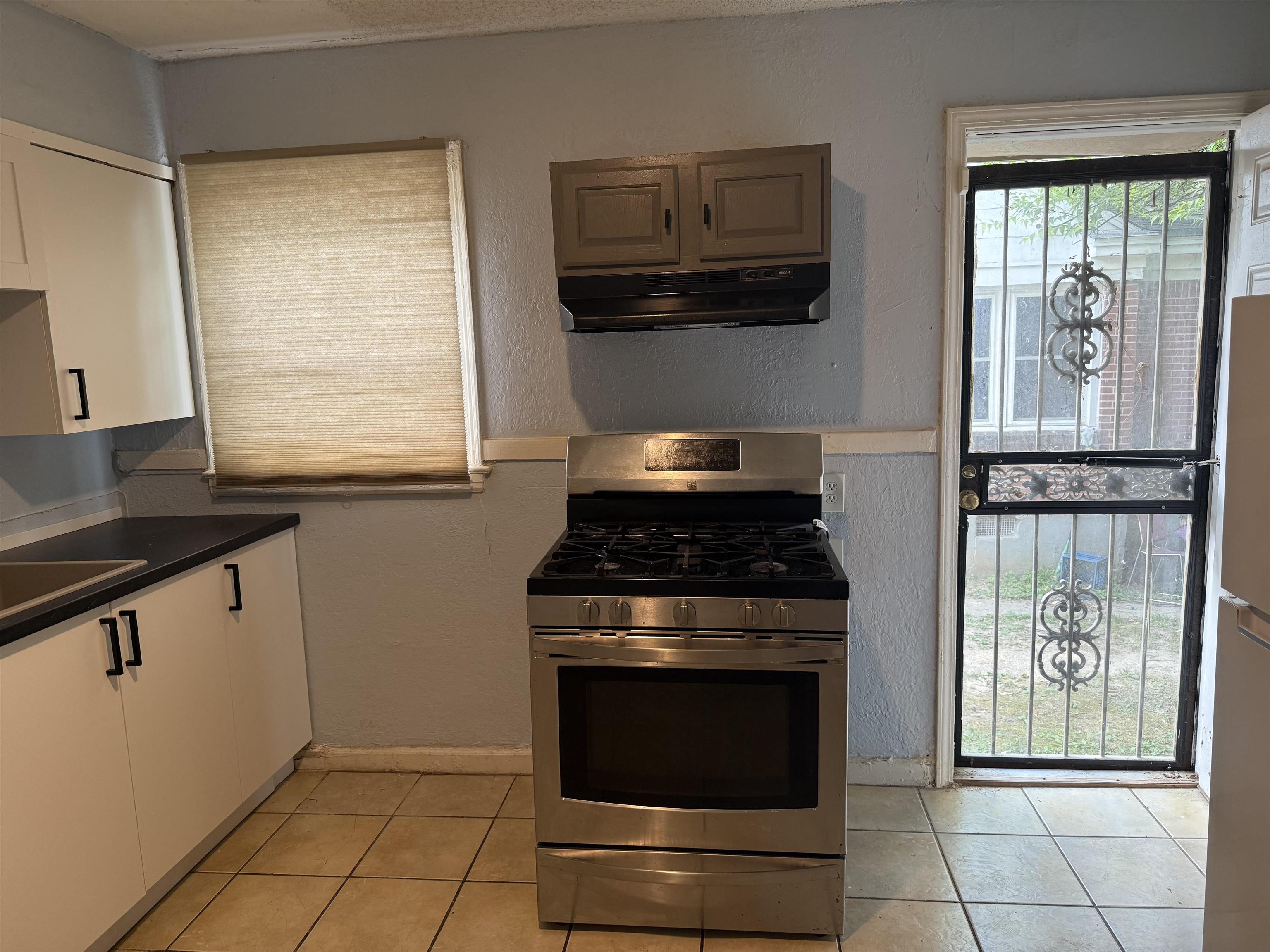 1248 Meda Street Memphis, TN 38114 - Photo 5 of 24 Kitchen featuring stainless steel range with gas stovetop, a textured wall, dark countertops, light tile patterned floors, and freestanding refrigerator